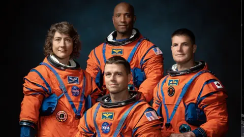 NASA Four Artemis II astronauts in their bright orange flight suits.